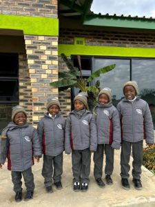 Five smiling students in grey winter jackets posing for a group photo.