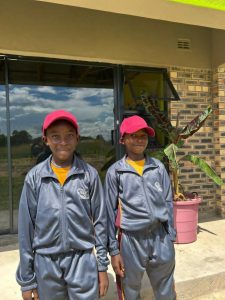 Two smiling boys in grey and gold sports tracksuits standing together.